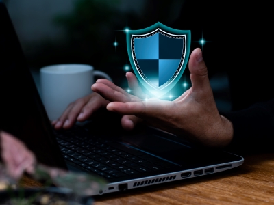 A businessman in front of a laptop is holding a shield protect symbol